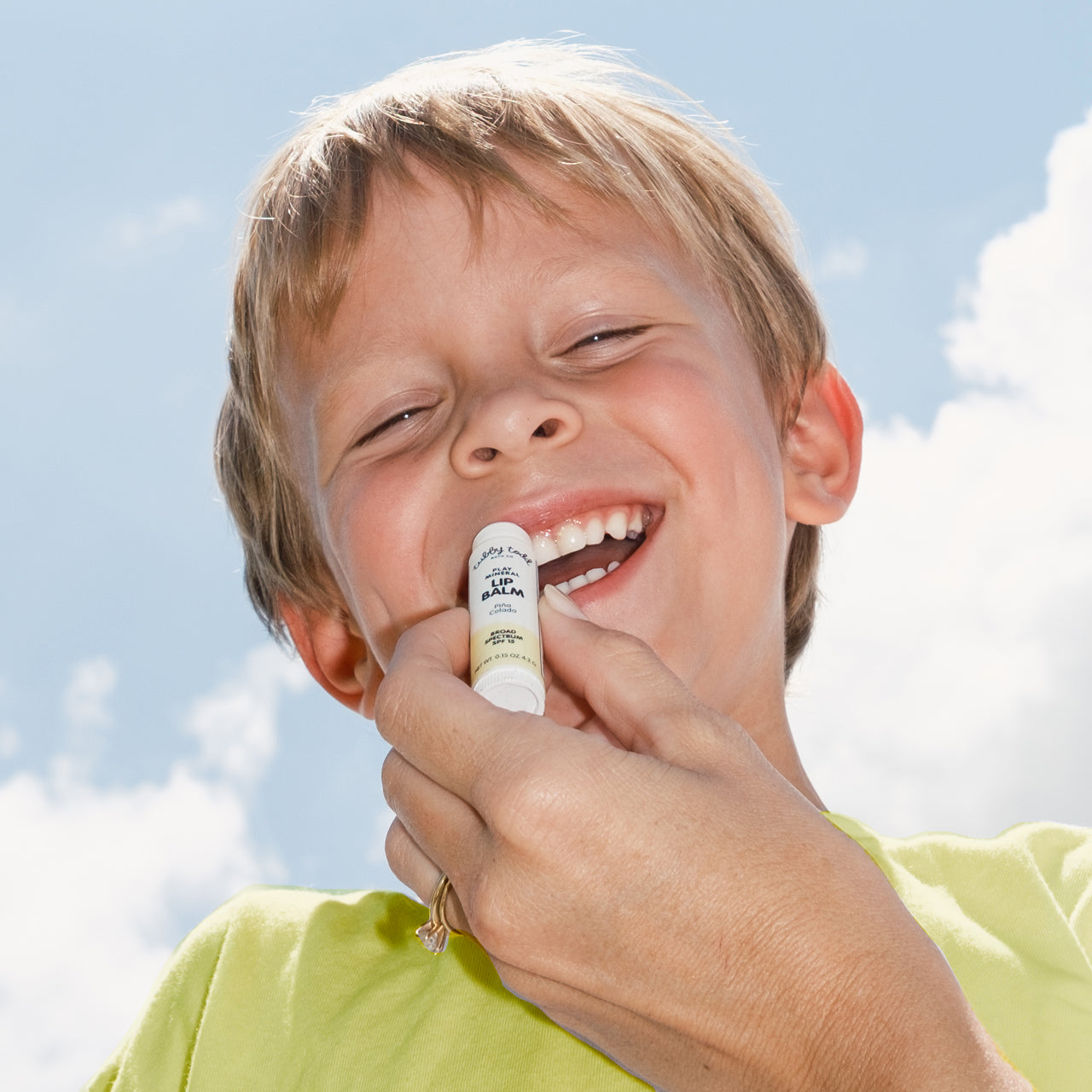 Hand applying sunscreen to a child against a blue sky background